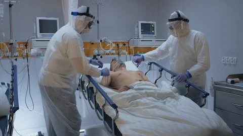 Doctors in Protective Suits Attaching ECG Leads to Coronavirus Patient Stock Footage 126528316