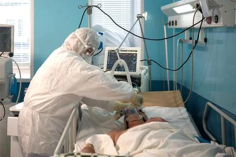 Doctors in protective suits put on a ventilation mask on a sick man with coro Stock Photos
