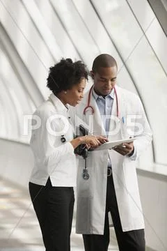 Doctors Using Digital Tablet In Hospital Corridor