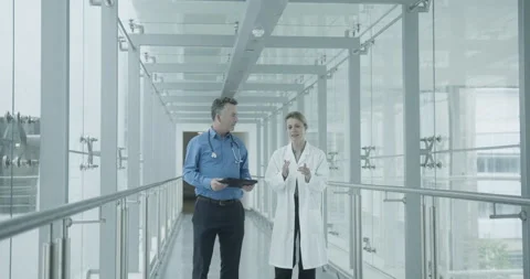 Doctors walking through hospital corridor discussing results on a digital tablet Stock Footage 158071706