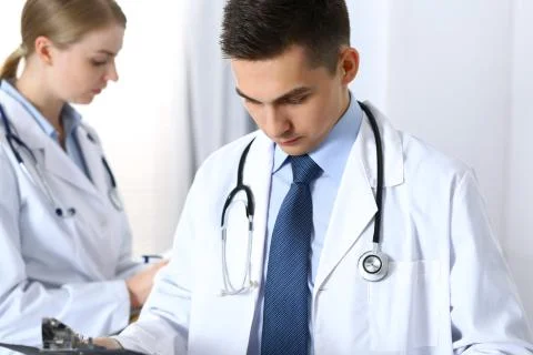Doctors writing papers using clipboard. Physicians discussing medication program 库存照片