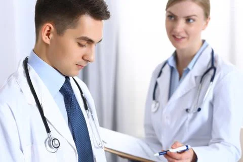 Doctors writing papers using clipboard. Physicians discussing medication program Stockfoto's