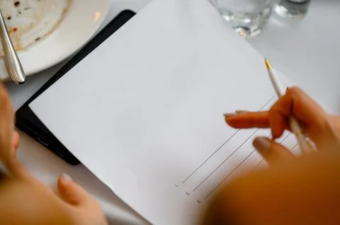 Document with text on table, hand holding pen, plate in background Stock Photos