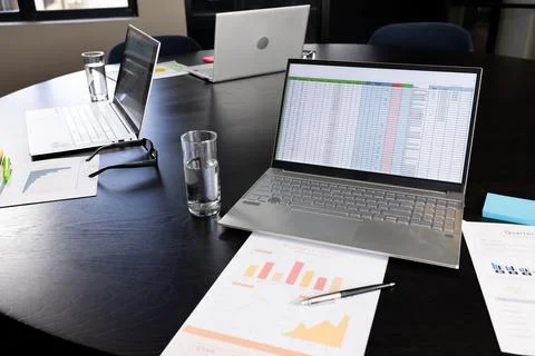 Documents and laptops, one with spreadsheet on screen, on table in office Stock Photos