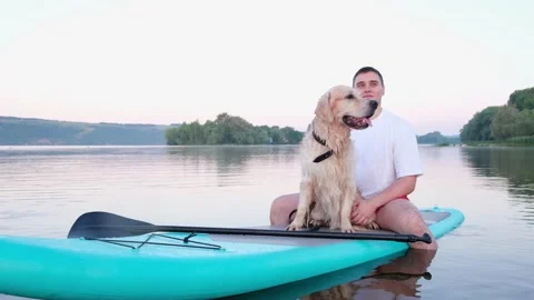 The dog sits on the paddleboard with the owner. Stock Footage 202315534