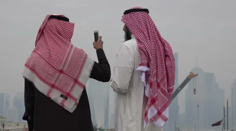 Doha, Qatar, two Saudi men take pictures of skyline and port Видео 49006761
