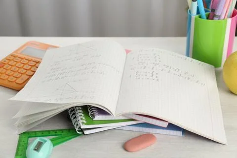 Doing homework. Notebook with assignment and stationery on white desk, closeu Stock Photos