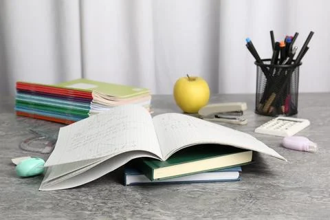 Doing homework. Notebook with math assignment, apple and stationery on grey.. Stock Photos
