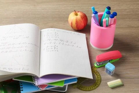 Doing homework. Notebook with math assignment, apple and stationery on wood.. Stock Photos