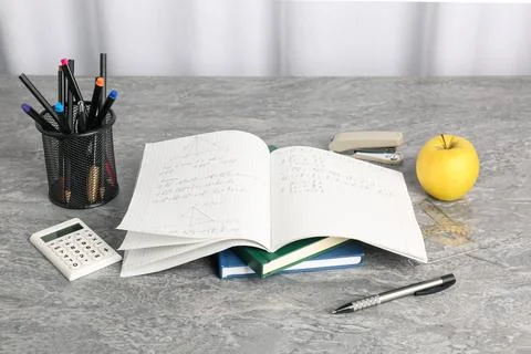 Doing homework. Notebook with math assignment, apple and stationery on grey.. Stock Photos