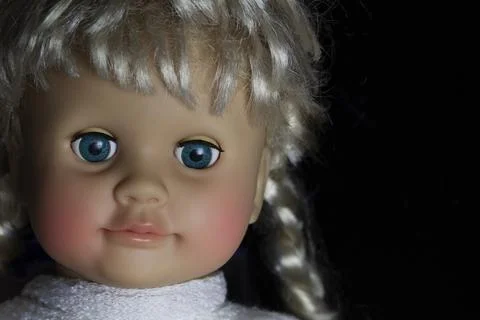 Doll face with bangs and pigtail close up in the dark. Stock Photos