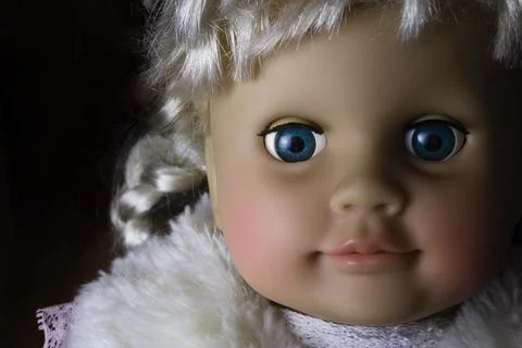 Doll portrait, plastic face with bangs and pigtail, close up in the dark. Stock Photos