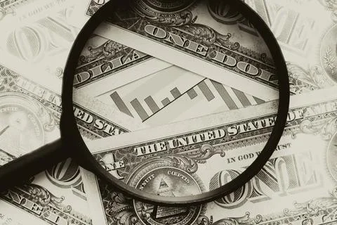 Dollars and currency chart under a magnifying glass close-up. Finance Stock Photos