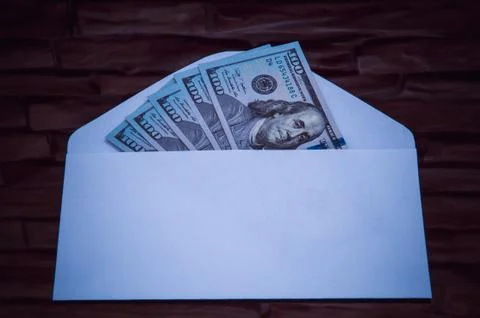 Dollars in an envelope against a dark brick wall. Stock Photos