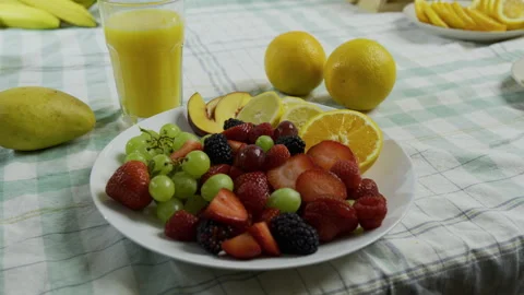 Dolly in and around plate of fruit with nearby cup of orange juice Stock Footage 341184196