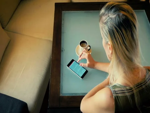 Dolly a blonde drinks cofee and reading an article in the phone. Stock Footage