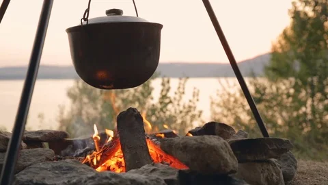 DOLLY MOTION: Brewed fish soup in an old pot. Cooking on fire near the lake Stockbeeldmateriaal 76201255