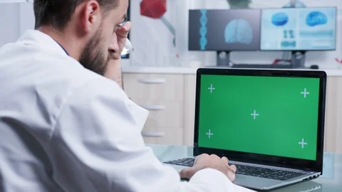 Dolly over the shoulder shot of practitioner working on green screen laptop Stock Footage 110902477