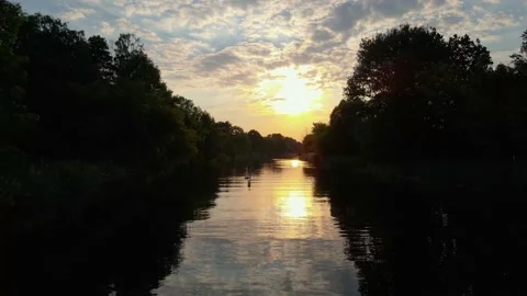 Dolly in over surface of water on river with trees at sunset with girl on SUP Stock Footage 159670979