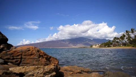 Dolly push in past volcanic rocks beach in Kihei Maui ocean West Maui Mountains Stock Footage 119086089