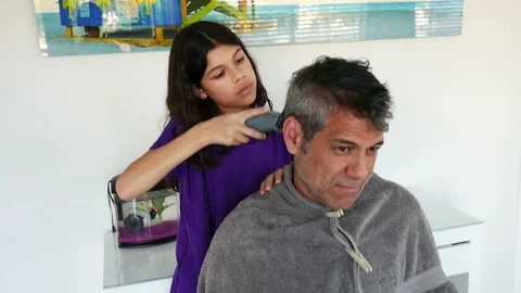 Dolly shot of 11-year-old girl cutting her father's hair during quarantine Stock Footage 129574166