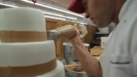 Dolly shot of a baker as he begins to apply icing on a cake Stock Footage 231414357
