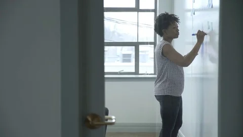 Dolly shot of businesswoman writing on white wall in board room at new office Stock Footage