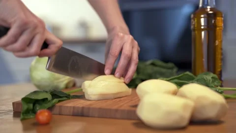 Dolly shot of camera. Slicing potatoes on a wooden cutting board. A woman's hand Vidéo 152651898