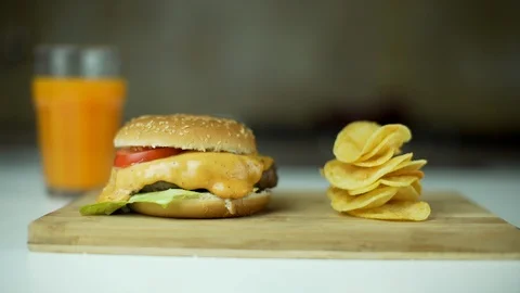 Dolly shot of cheeseburger, a stack of chips,  a glass of orange juice. Stock Footage 101965670