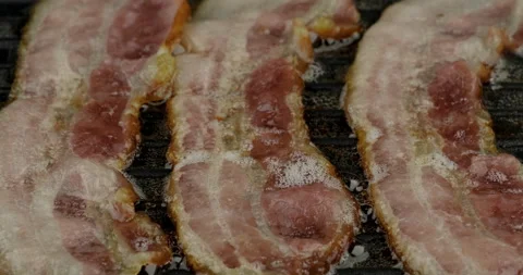 Dolly shot close up of crispy bacon frying grill on non-stick enamel pan grill Stock Footage 145451634