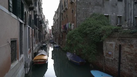 Dolly shot of covered boats moored on canal amidst residential buildings against Stock Footage