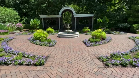 Dolly shot down flowered brick path to reveal garden fountain Stock Footage 239100871