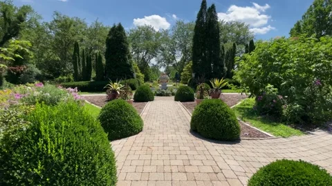 Dolly shot down flowered path revealing garden centerpiece Stock Footage 239075191