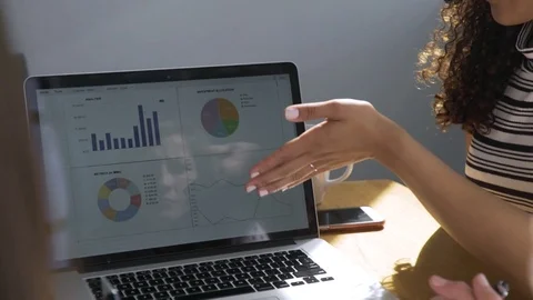 Dolly shot of female colleagues discussing graphs over laptop computer in board Stock Footage