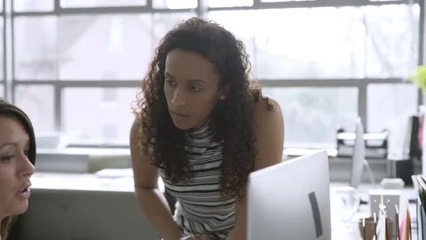 Dolly shot of female colleagues discussing over desktop computer in office Stock Footage