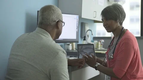 Dolly shot of female doctor explaining reports on tablet computer to patient in Stock Footage