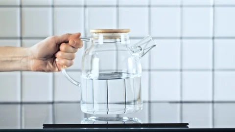 Dolly shot of female hand putting glass teapot on the induction cooker Stock Footage 89651653
