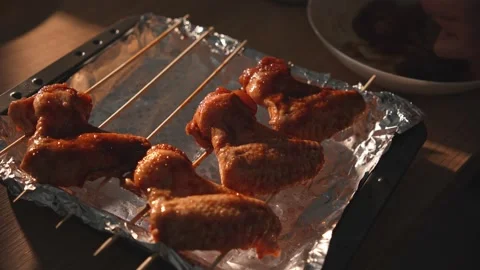 Dolly shot of hands arranging marinated wings on foil-lined tray Stock Footage 312647949