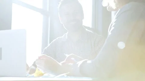 Dolly shot of happy colleagues discussing while sitting at table in office Stock Footage