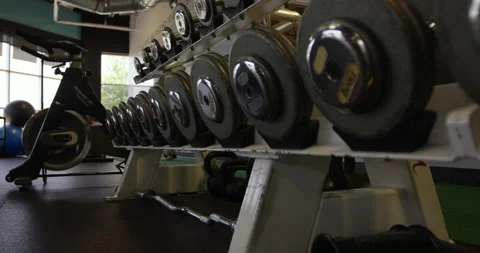 Dolly shot in on rack of weights and a stationary bike in gym Stock Footage 148246408