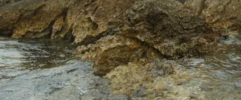 Dolly shot on seashore, small waves crushing on rocks in slowmotion Stock Footage 97899252