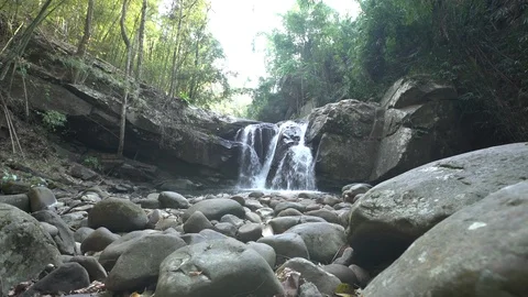 Dolly tracking shot of waterfall in rainforest with rocks in foreground Stock Footage 87188372
