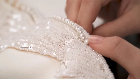 A dolly of woman's hands sewing beaded lace down the wedding dress Video stock 99047558