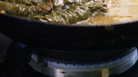 Dolma with meat in grape leaves is stewed in a frying pan in meat broth over a Stock Footage 309347668