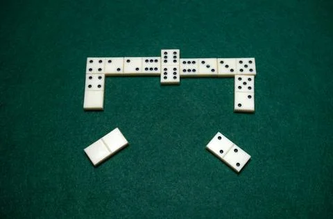 Dominoes are arranged on a green table, some tiles form a line and others a.. Stock Photos