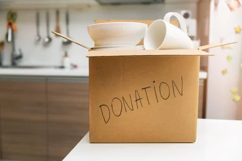 Donate household items - box with tableware for donation on kitchen table Stock Photos