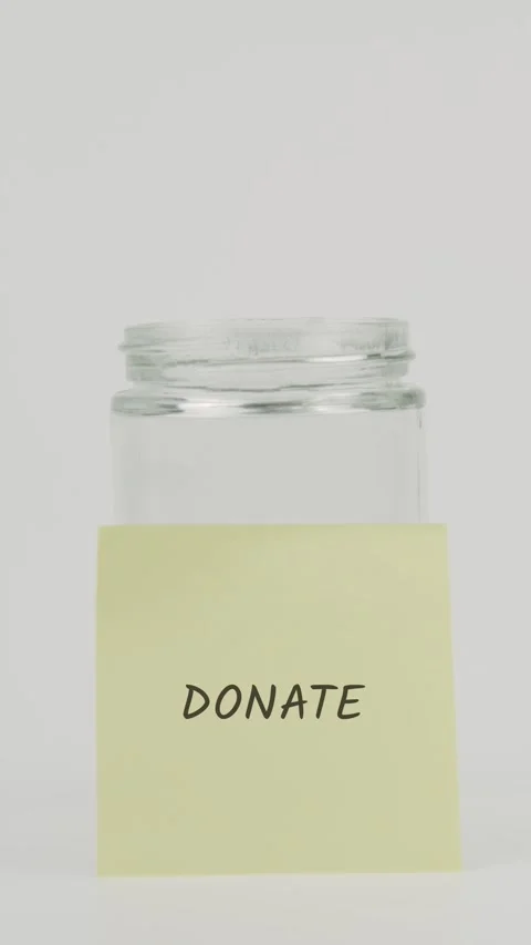 Donate text or word on yellow sticky note attached to glass jar with hand Stock Footage 311721048