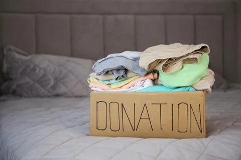 Donation box with clothes on the bed. Stock Photos