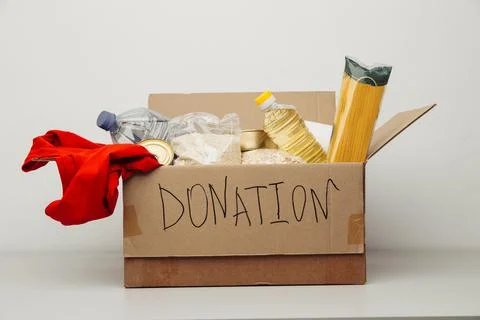 Donation box. Open cardboard box with clothes and food on a white background Stock Photos