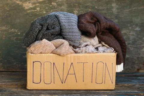 Donation box with warm things on old wooden background. Stock Photos
